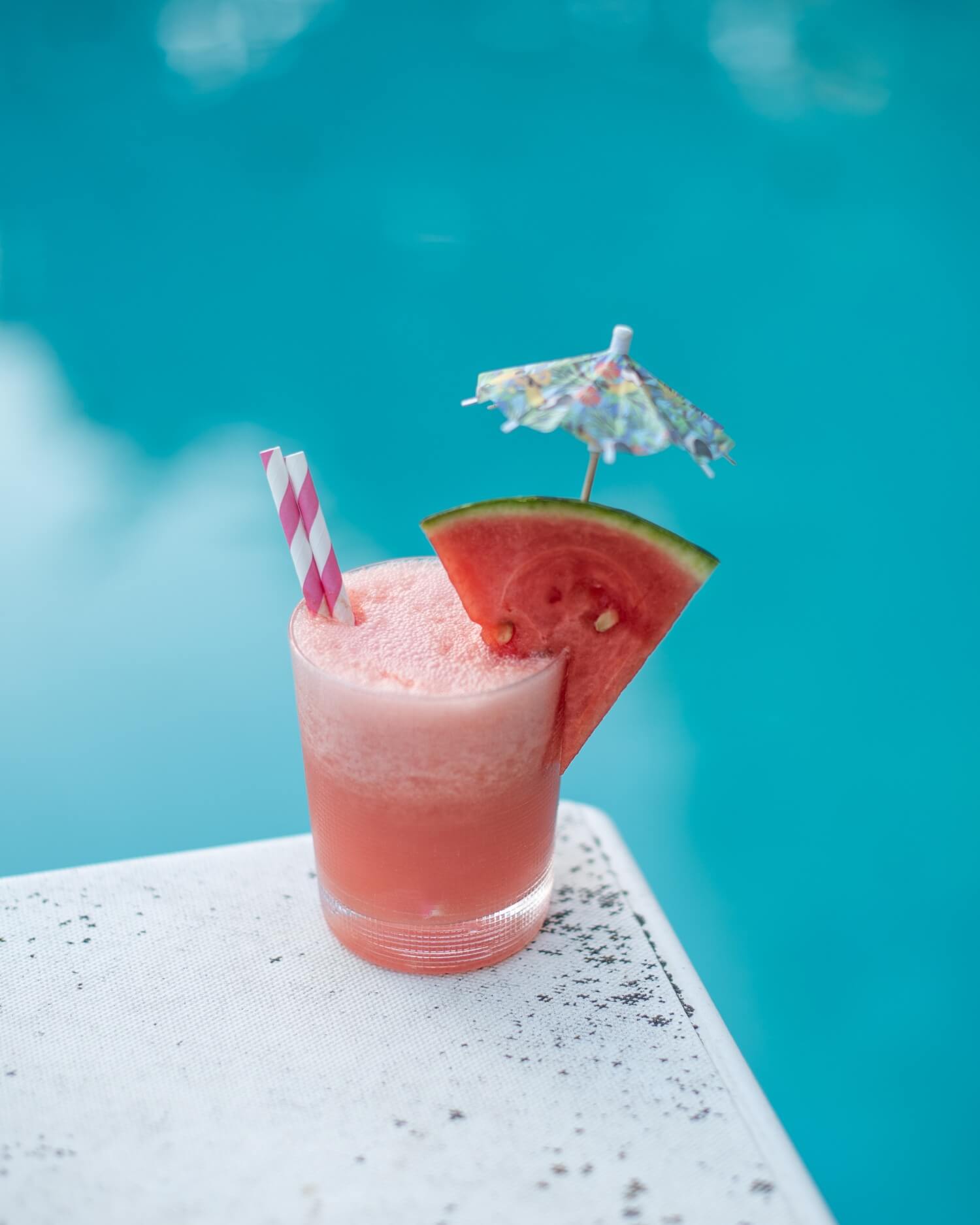 a watermelon mai-tai cocktail on the edge of a diving board by the pool
