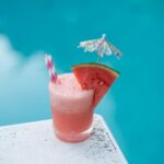a watermelon mai-tai cocktail on the edge of a diving board by the pool